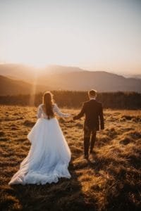 a married couple walk through a golden field at twilight on their wedding day