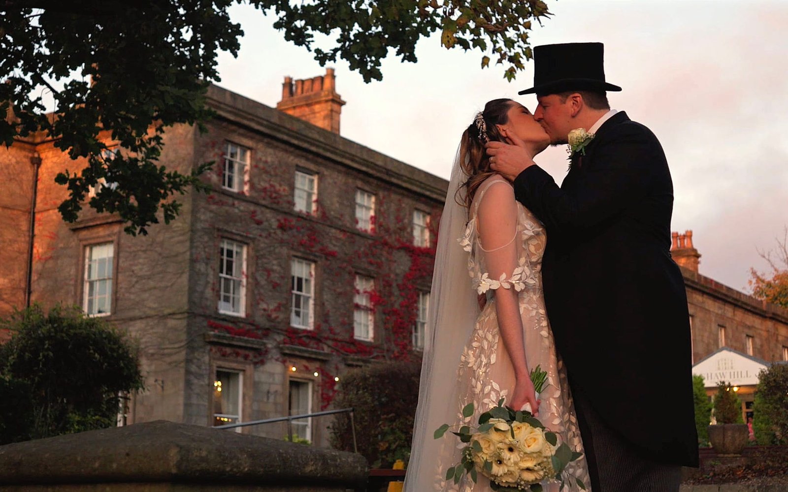A twilight wedding filmed in Lancashire a bride and groom kiss at their wedding day with a twilight sunset in front of a stately home